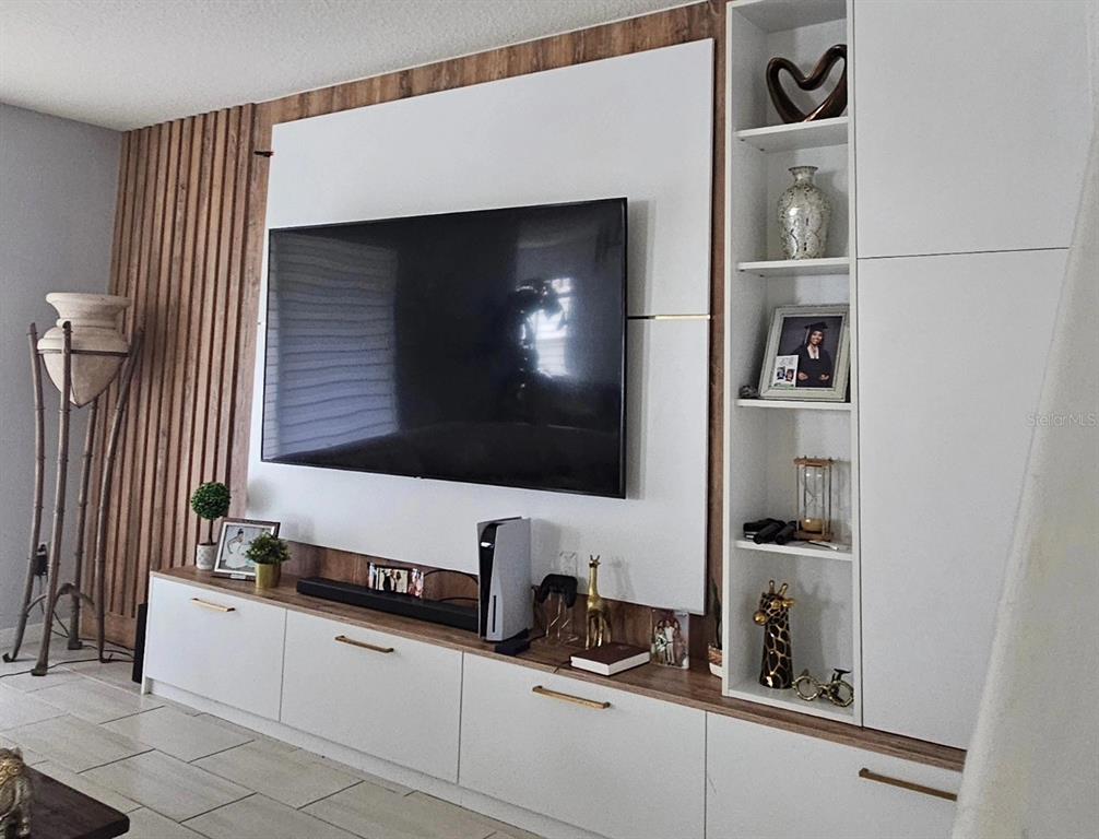 A wall-mounted television is centered above a white and wood-toned media console with shelving — 15929 MOONLIGHT BAY STREET, WINTER GARDEN, FL