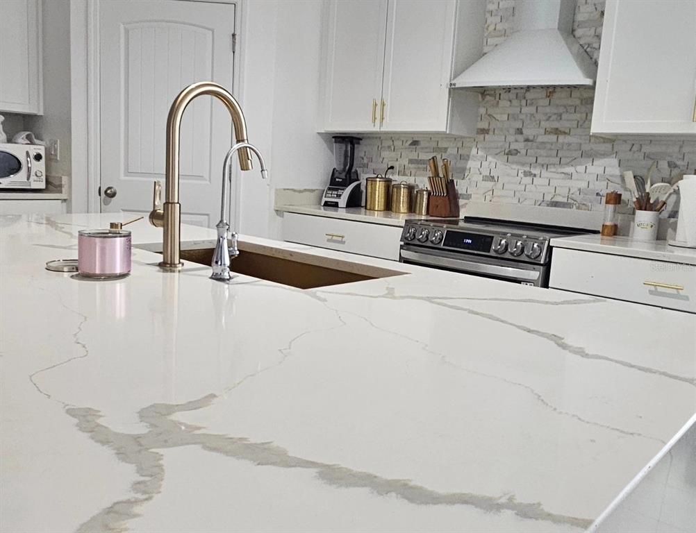 A modern kitchen features a large white quartz island with a gold faucet and sink — 15929 MOONLIGHT BAY STREET, WINTER GARDEN, FL