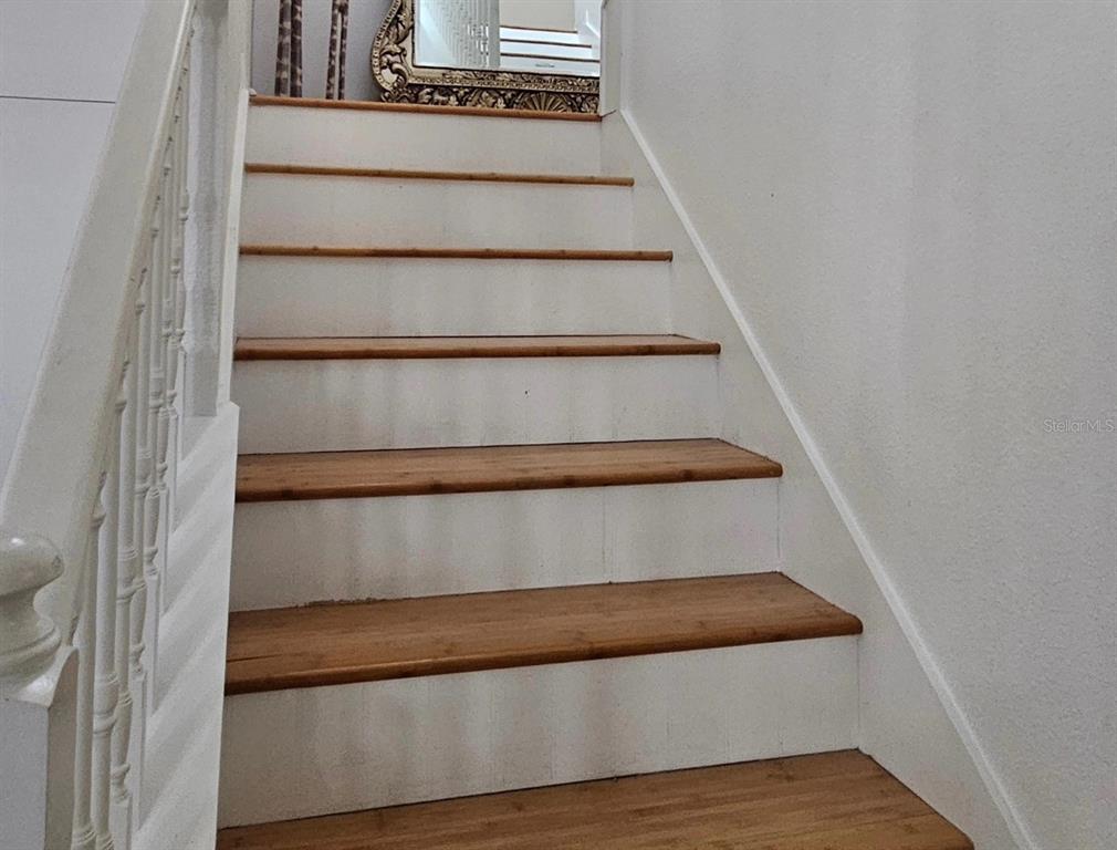 A staircase with wooden treads and white risers leads to a landing with a mirror — 15929 MOONLIGHT BAY STREET, WINTER GARDEN, FL