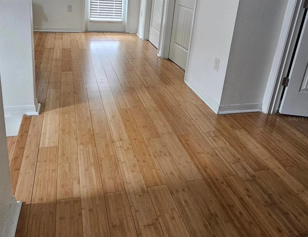 A hallway with light-colored bamboo flooring leads toward a window with white blinds — 15929 MOONLIGHT BAY STREET, WINTER GARDEN, FL