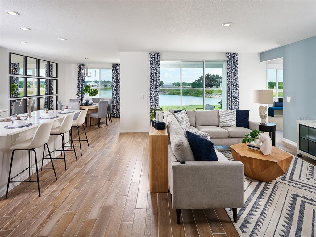 An open-concept living and dining area features wood-look tile flooring and views of a lake — 14152 HARVEST PINES LANE, HUDSON, FL