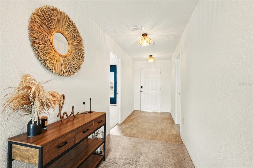 A bright entryway features a wood console table, a circular wall mirror, and light flooring — 1409 NE 4TH PLACE, CAPE CORAL, FL