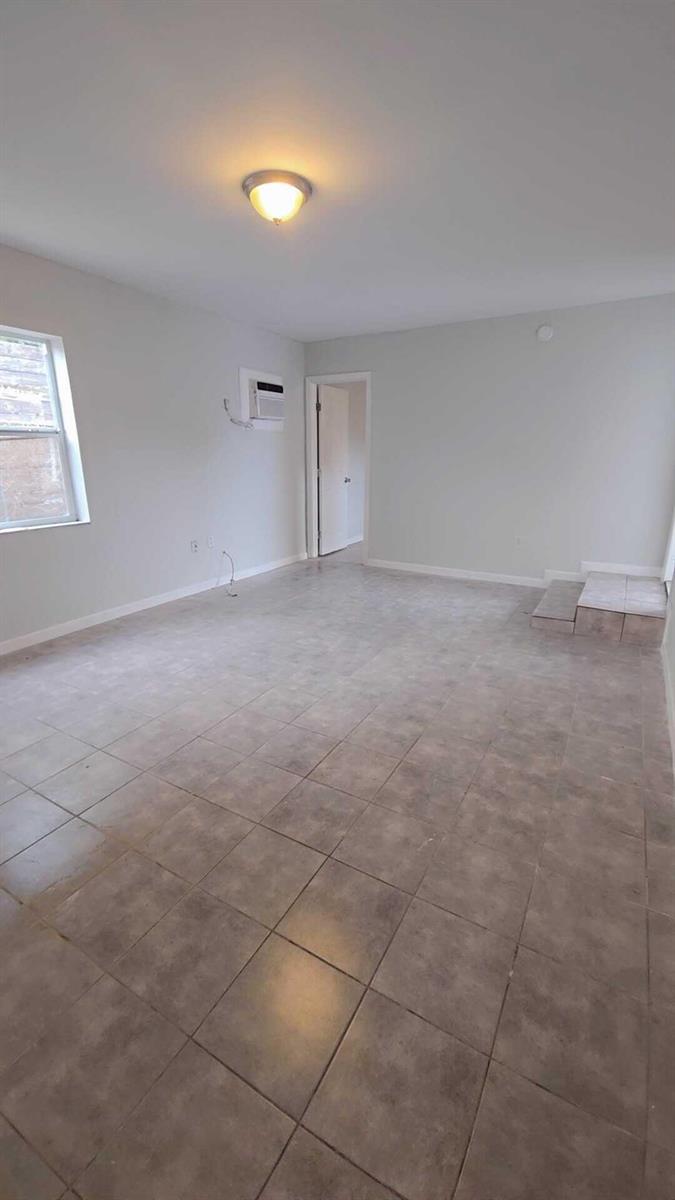 An empty room features light gray walls, tiled flooring, a window, and a wall-mounted air conditioner — 621 NW 5th Avenue Unit 3, Pompano Beach FL 33060, POMPANO BEACH, FL