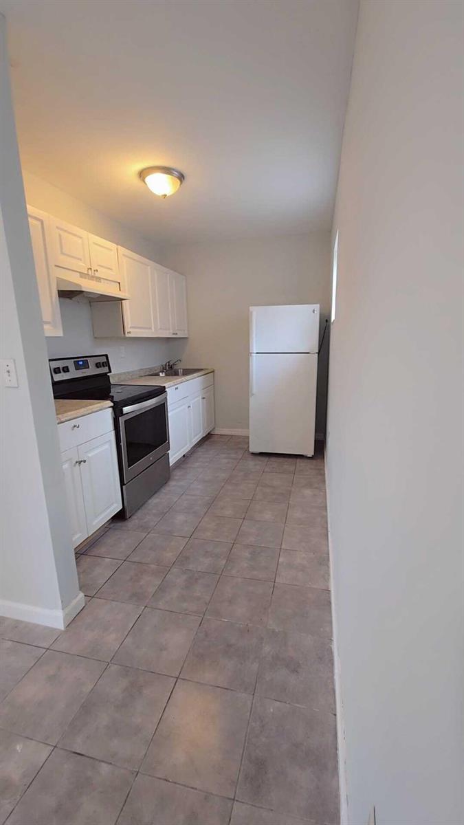 A galley kitchen features white cabinets, stainless steel appliances, and light-colored tile flooring — 621 NW 5th Avenue Unit 3, Pompano Beach FL 33060, POMPANO BEACH, FL