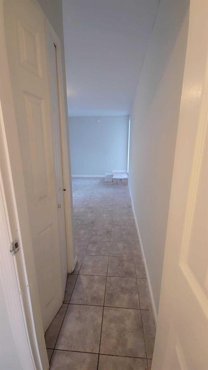 A narrow hallway with light-colored tile flooring leads toward an open room with a step — 621 NW 5th Avenue Unit 3, Pompano Beach FL 33060, POMPANO BEACH, FL