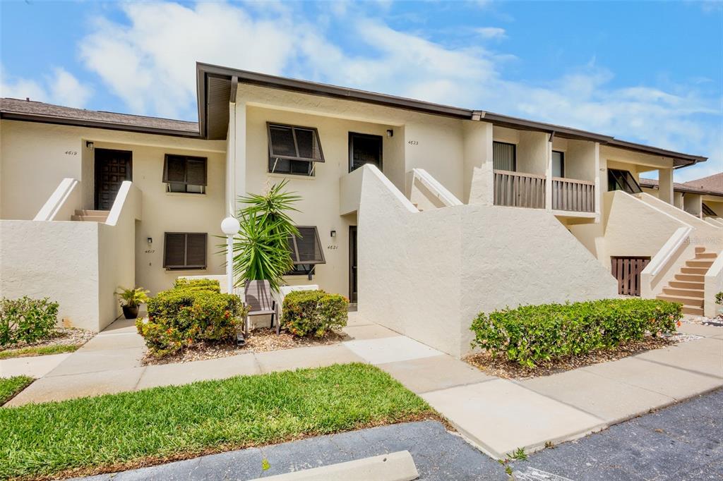 A two-story stucco apartment building features multiple entrances, outdoor staircases, and small landscaped front gardens — 4623 LONGWATER CHASE 112 Bldg J, SARASOTA, FL