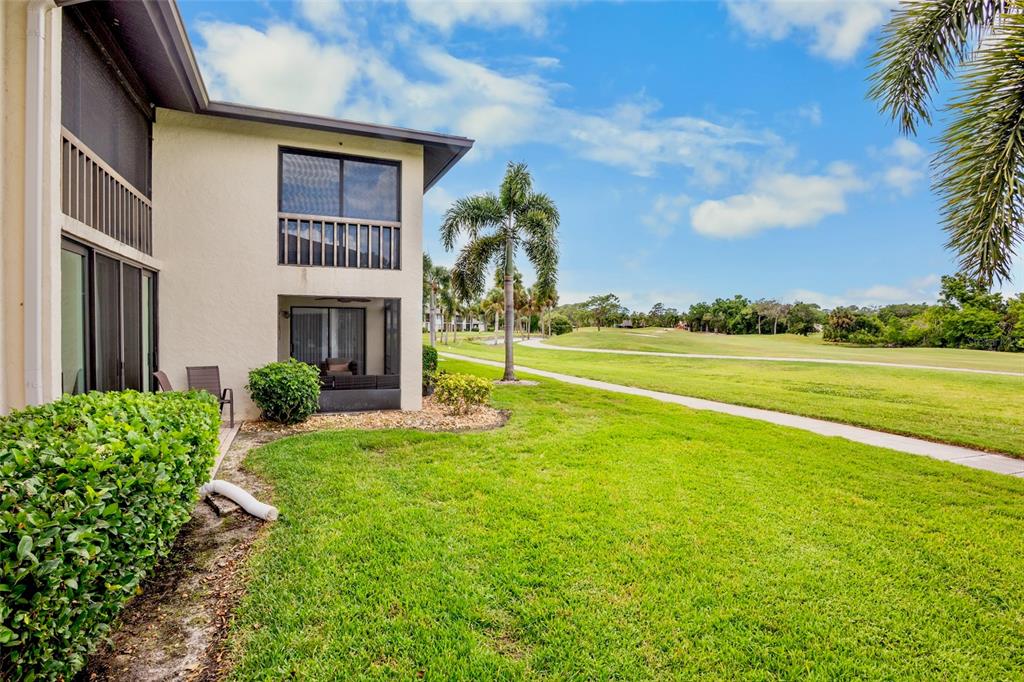 A two-story building with screened balconies overlooks a grassy golf course under a blue sky — 4623 LONGWATER CHASE 112 Bldg J, SARASOTA, FL