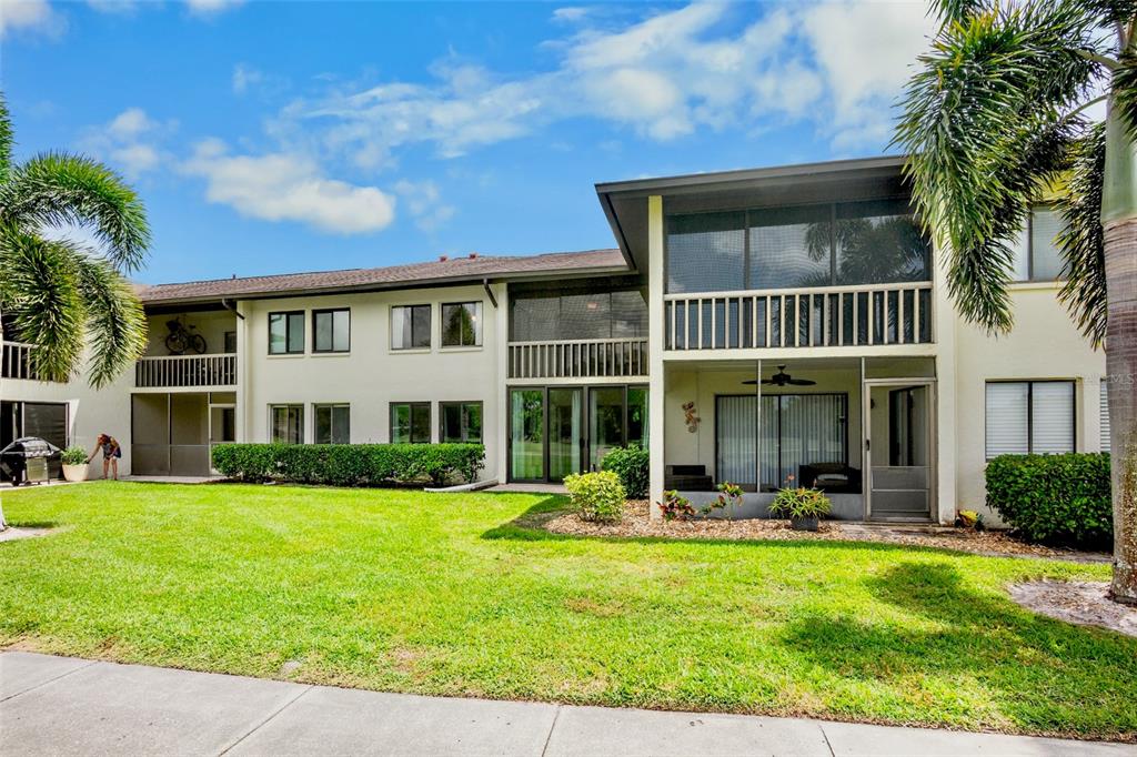 A two-story apartment building with screened balconies and a grassy lawn in the foreground — 4623 LONGWATER CHASE 112 Bldg J, SARASOTA, FL