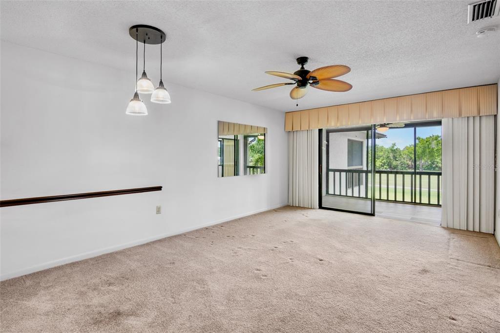 A carpeted living room features a ceiling fan, pendant lights, and a sliding glass door — 4623 LONGWATER CHASE 112 Bldg J, SARASOTA, FL