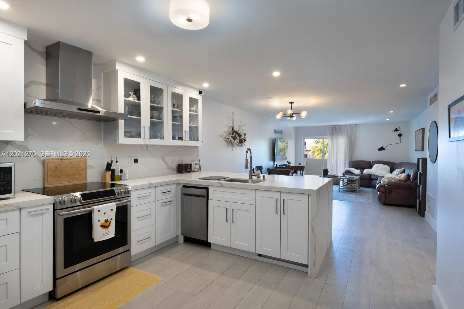 A modern kitchen with white cabinets and marble countertops opens into a living area — 6815 Edgewater Dr # 307, Coral Gables FL 33133, CORAL GABLES, FL