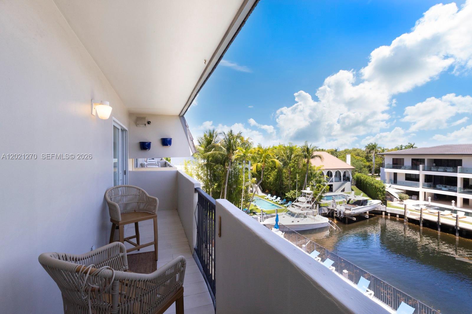 A balcony with two wicker chairs overlooks a canal, boats, and a swimming pool — 6815 Edgewater Dr # 307, Coral Gables FL 33133, CORAL GABLES, FL