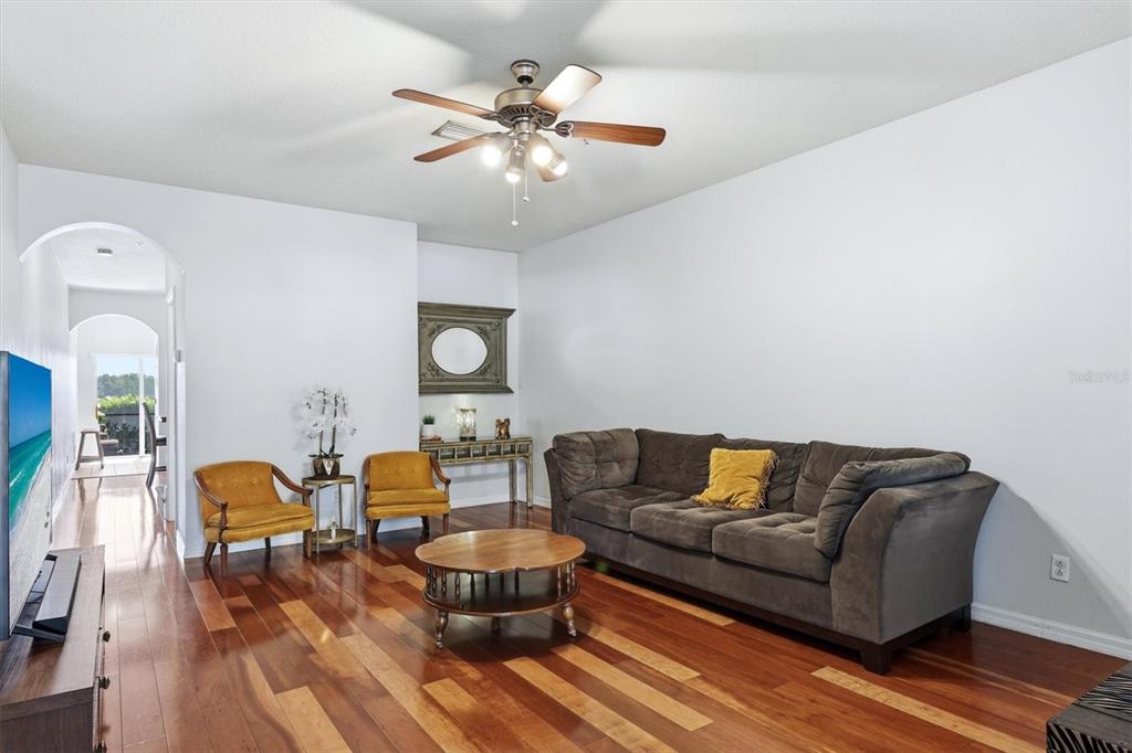 A living room features hardwood floors, a brown sofa, two yellow chairs, and a ceiling fan — 3903 45TH TERRACE W UNIT 106, BRADENTON, FL