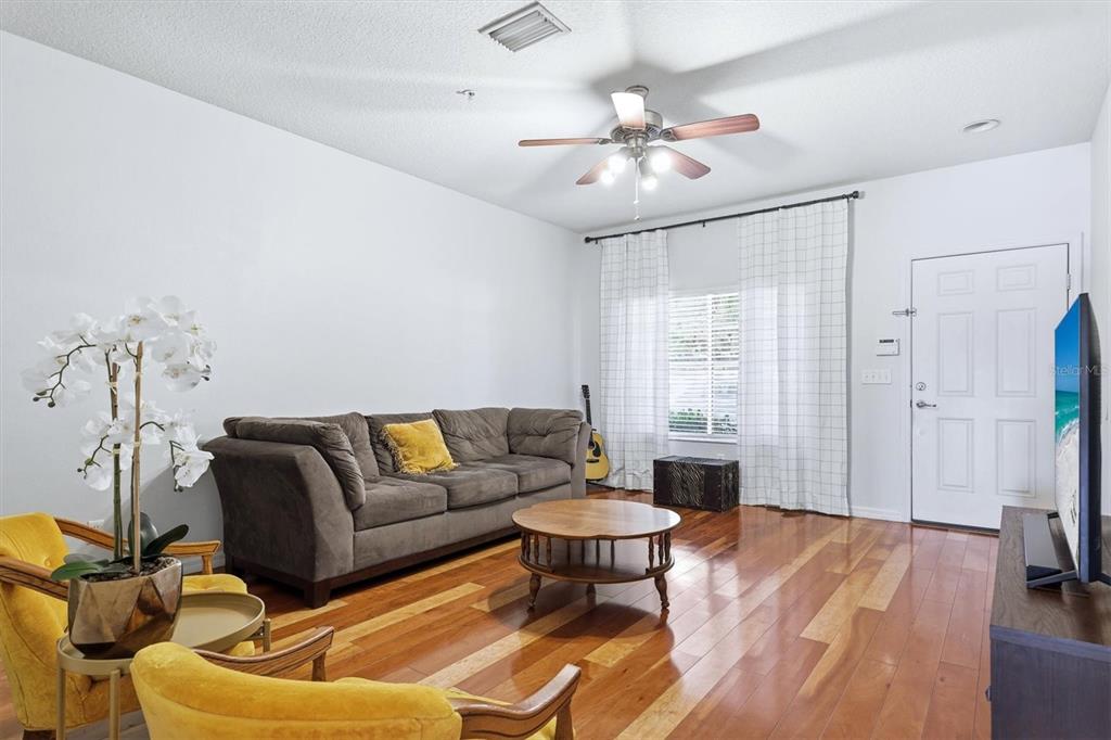 A living room features hardwood floors, a brown sofa, yellow armchairs, and a ceiling fan — 3903 45TH TERRACE W UNIT 106, BRADENTON, FL
