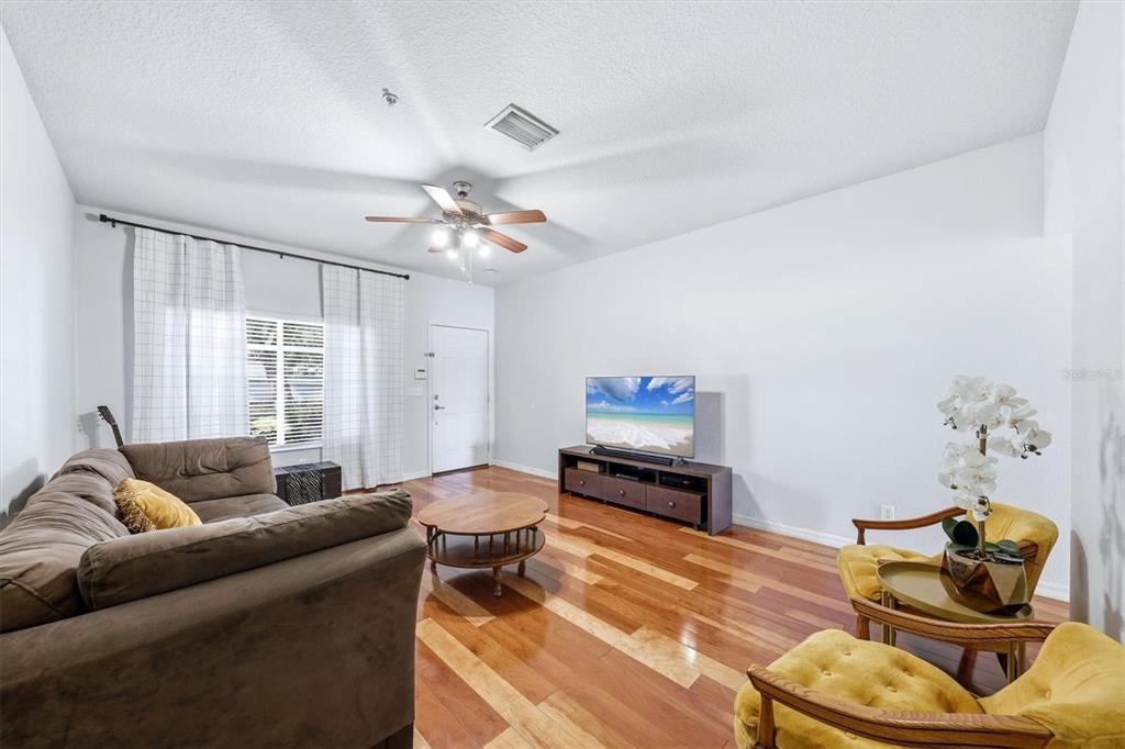A living room features hardwood floors, a brown sofa, two yellow chairs, and a television — 3903 45TH TERRACE W UNIT 106, BRADENTON, FL