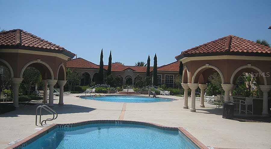 An outdoor swimming pool area features two covered gazebos and a large clubhouse building — 5566 METROWEST BOULEVARD UNIT 2-106, ORLANDO, FL