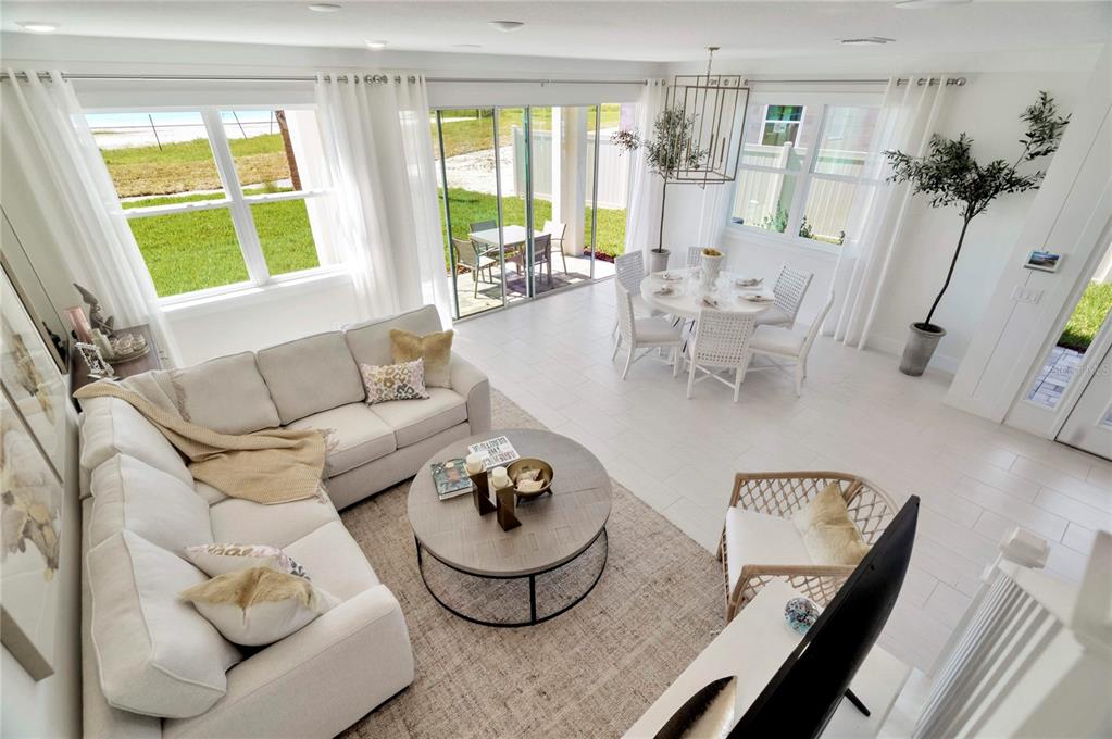 A bright, open-concept living and dining area features white tile floors, neutral furniture, and sliding doors — 32062 ANCHOR POINT DRIVE, WESLEY CHAPEL, FL