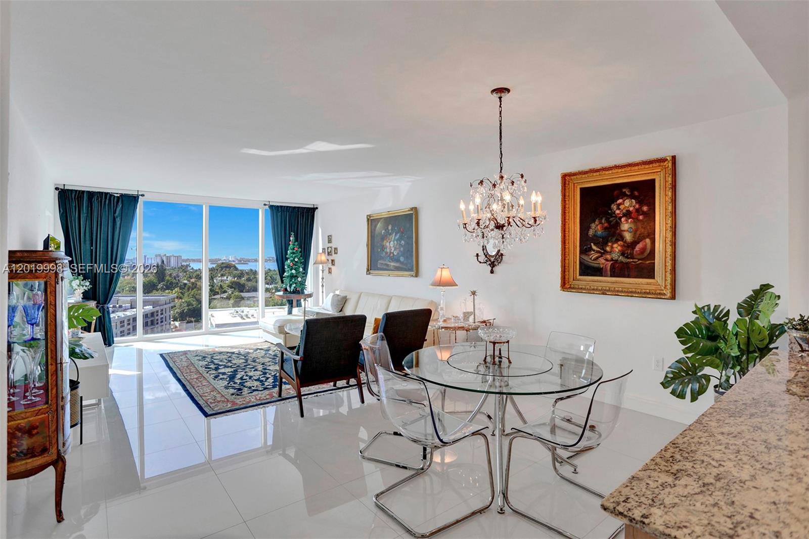 A bright living and dining area features white tile floors, a crystal chandelier, and floor-to-ceiling windows — 10275 Collins Ave # 829, Bal Harbour FL 33154, BAL HARBOUR, FL