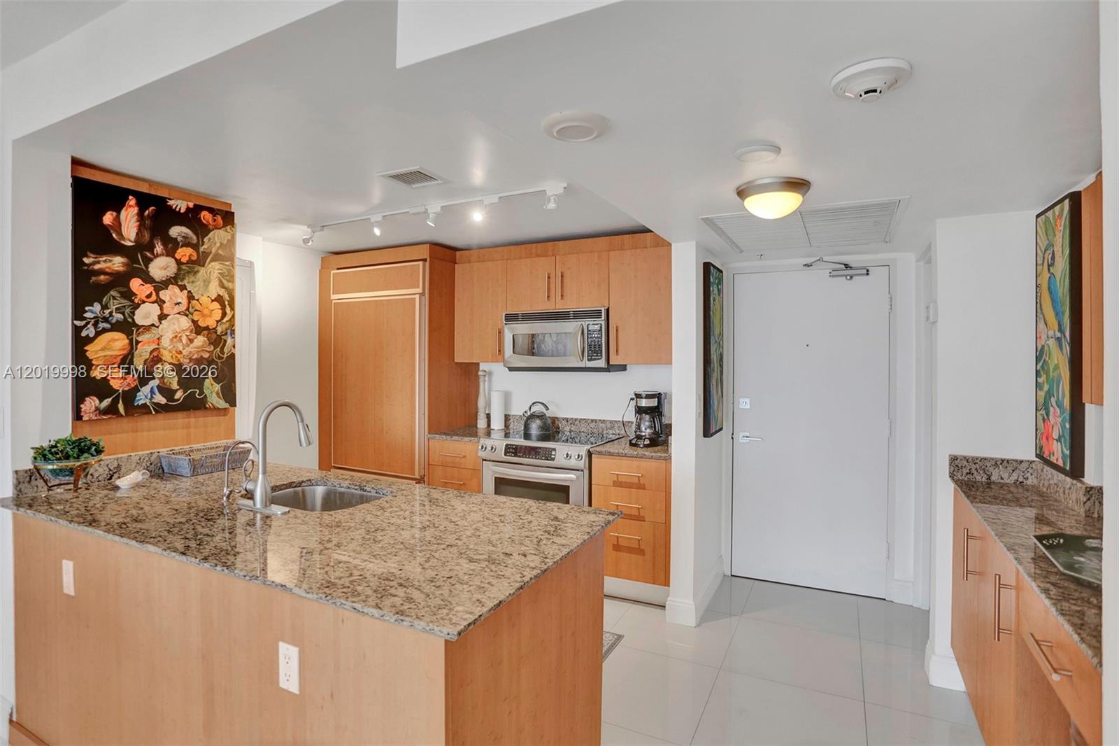 A kitchen features light wood cabinets, granite countertops, a kitchen island, and stainless steel appliances — 10275 Collins Ave # 829, Bal Harbour FL 33154, BAL HARBOUR, FL