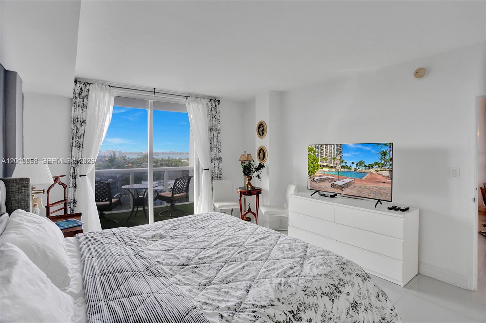 A bedroom features a bed, white dresser with a television, and a balcony with views — 10275 Collins Ave # 829, Bal Harbour FL 33154, BAL HARBOUR, FL