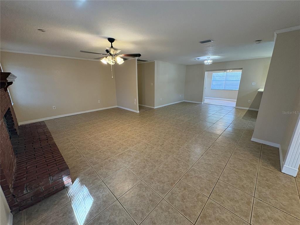 A spacious living room features tan tile flooring, a brick fireplace, and a ceiling fan — 8351 WAKEFORD ROAD, LAKE WALES, FL