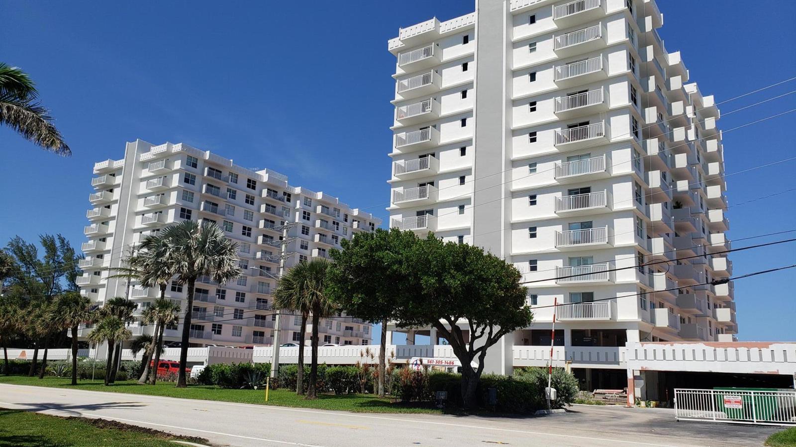 Two tall white residential buildings stand behind a grassy area with palm trees and shrubs — 4511 S Ocean Boulevard # 904, Highland Beach FL 33487, HIGHLAND BEACH, FL