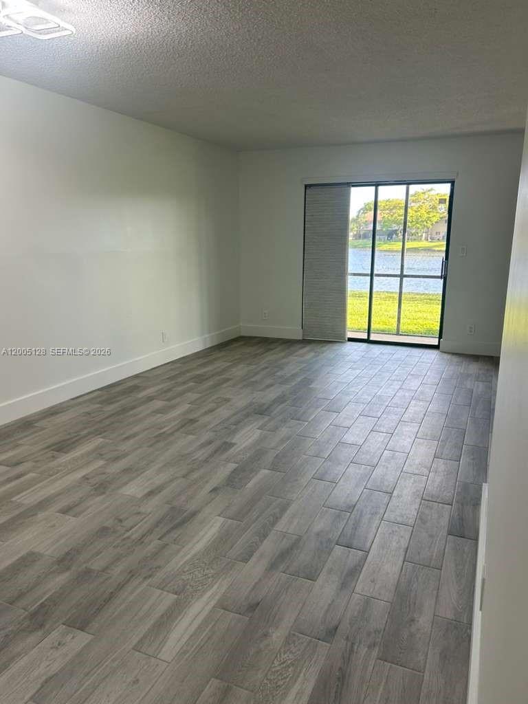An empty room features gray wood-look tile flooring and a sliding glass door to water — 9926 Nob Hill Ct # 9926, Sunrise FL 33351, SUNRISE, FL