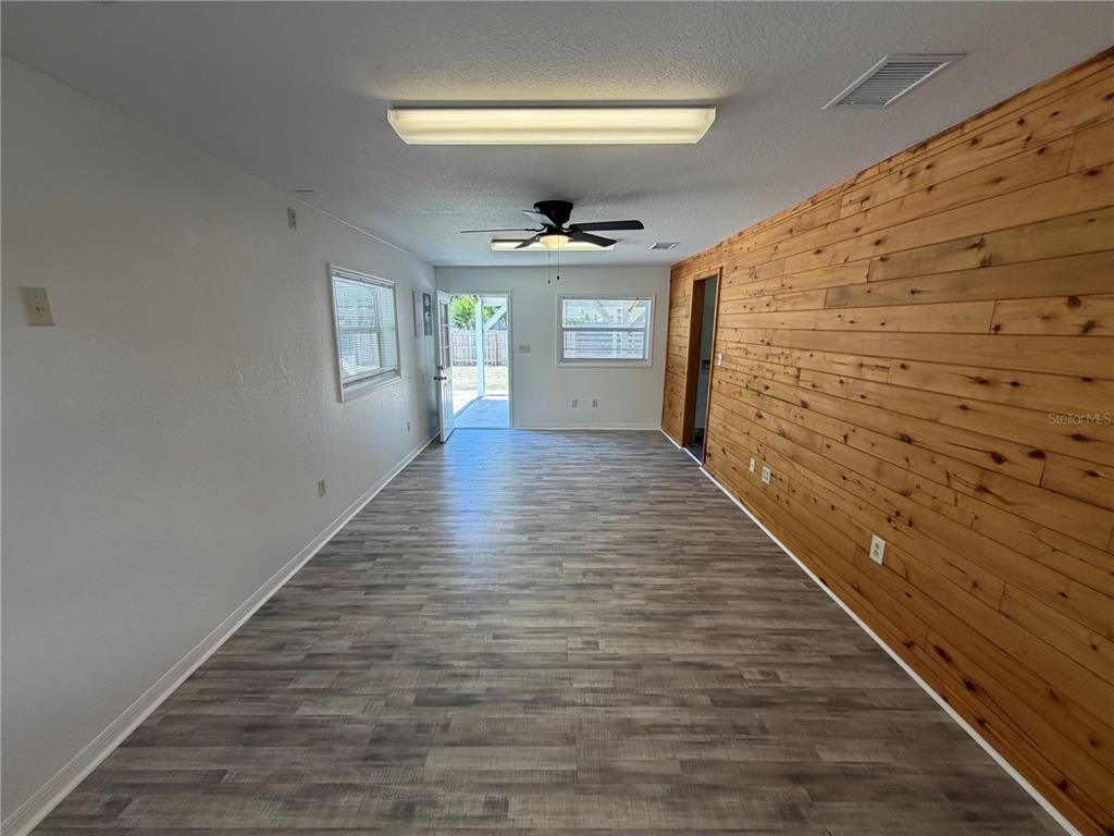 A long room features wood-paneled walls, gray wood-look flooring, a ceiling fan, and an exterior door — 306 N IONA AVENUE, FRUITLAND PARK, FL