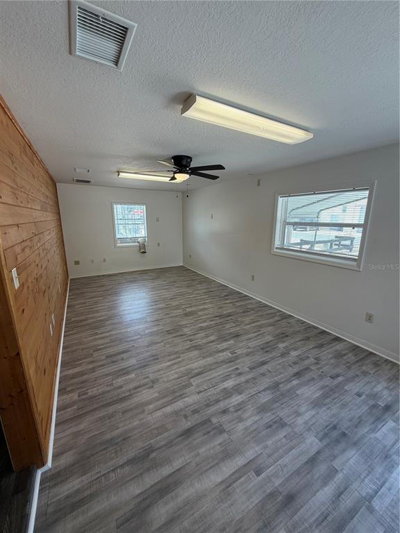 A room with wood-paneled walls, gray wood-look flooring, a ceiling fan, and two windows — 306 N IONA AVENUE, FRUITLAND PARK, FL