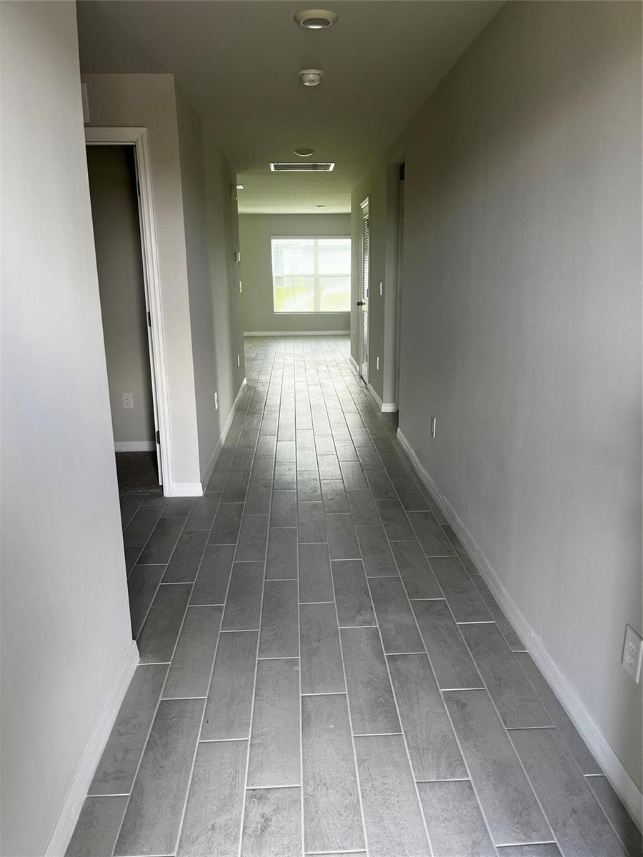 A hallway with gray wood-look tile flooring leads toward a window at the far end — 4021 35th Street, Lehigh Acres FL 33976, LEHIGH ACRES, FL