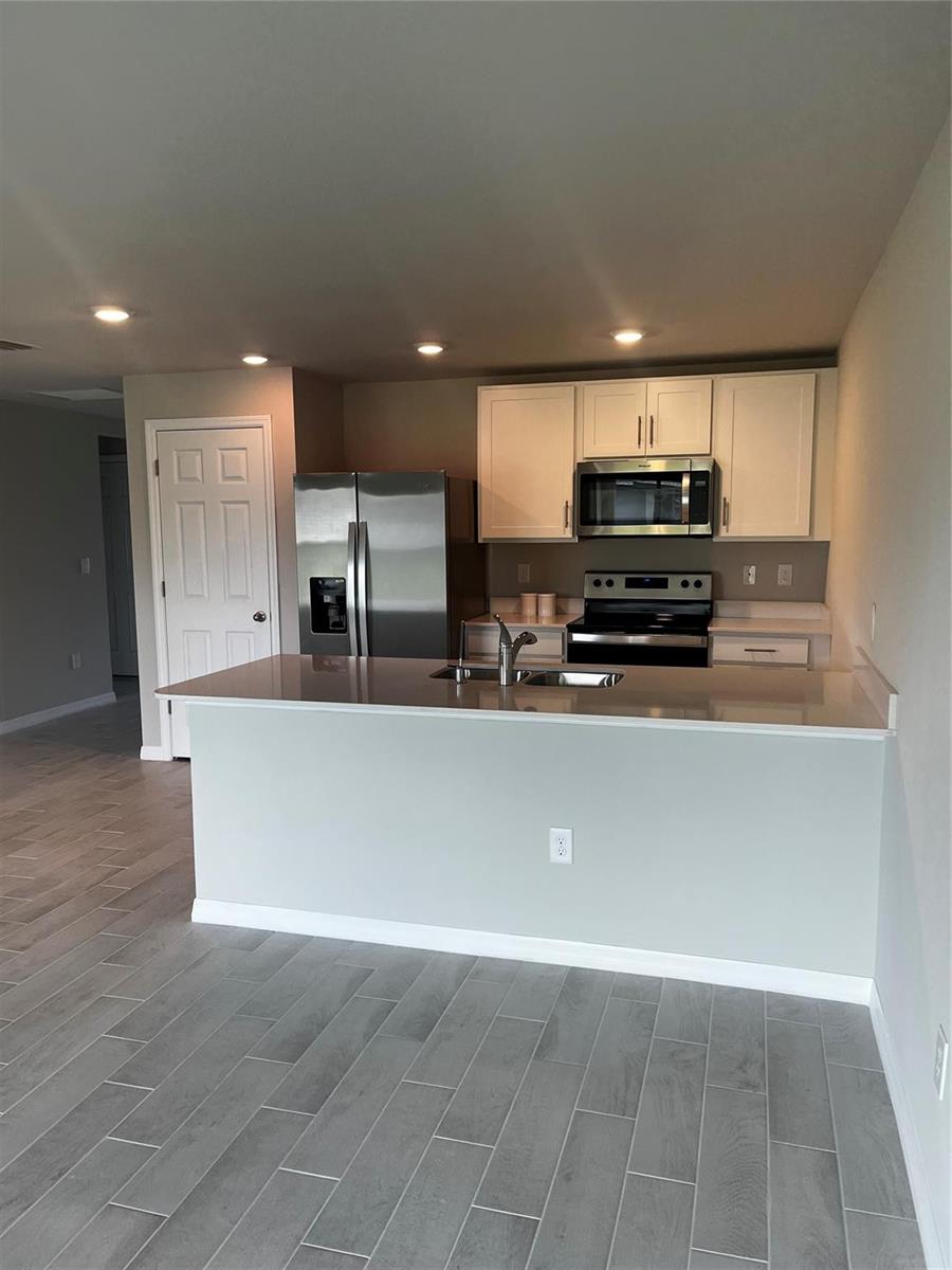 A kitchen features white cabinets, stainless steel appliances, a breakfast bar, and gray tile flooring — 4021 35th Street, Lehigh Acres FL 33976, LEHIGH ACRES, FL