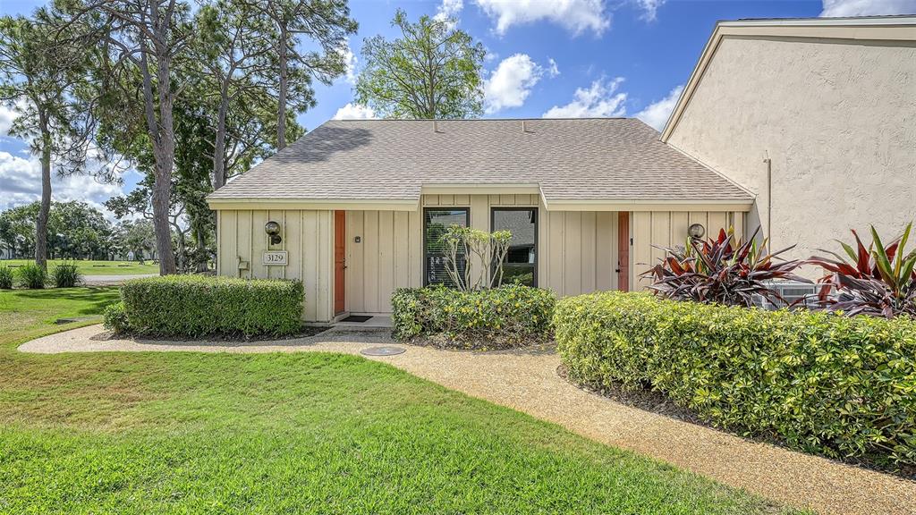 A tan, single-story duplex with a gravel walkway and manicured hedges under a blue sky — 3127 LONGMEADOW UNIT 2, SARASOTA, FL