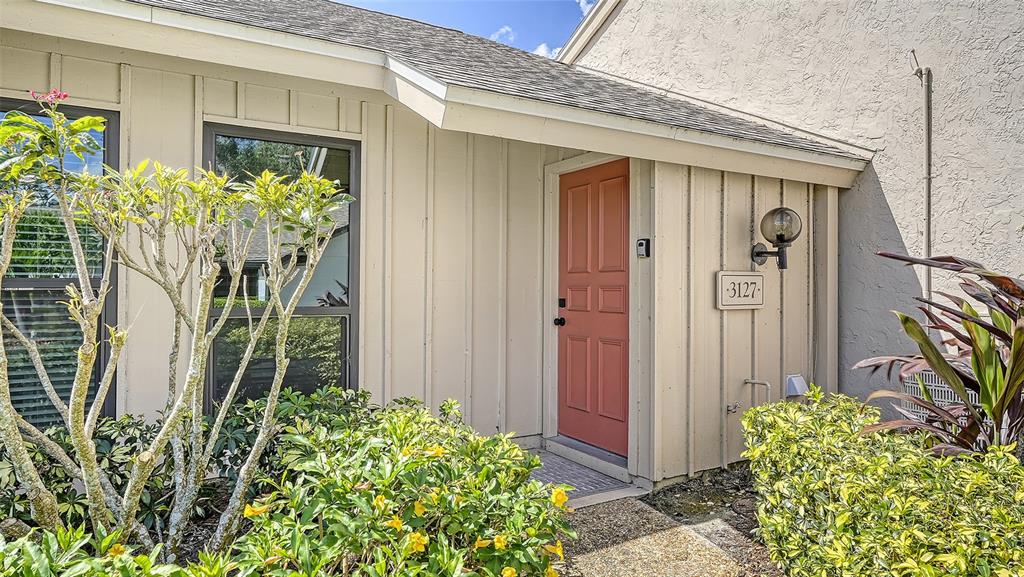 The exterior of a home features a red front door, beige siding, and landscaping — 3127 LONGMEADOW UNIT 2, SARASOTA, FL