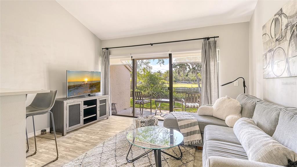 A living room features a gray sectional sofa, a glass coffee table, and sliding glass doors — 3127 LONGMEADOW UNIT 2, SARASOTA, FL