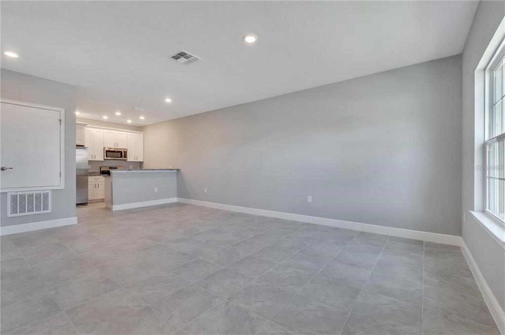 An open-concept living area with gray tile flooring leads to a kitchen with white cabinets — 1746 CORIANDER DRIVE UNIT 1746, KISSIMMEE, FL