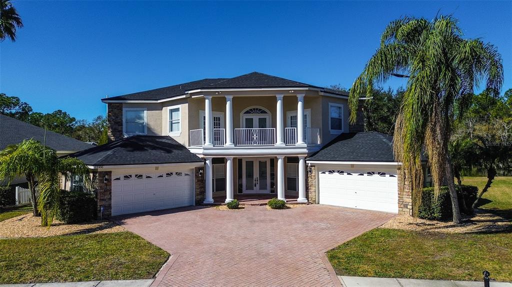 A two-story house with a brick driveway, two garages, and a second-floor balcony with columns — 15906 PRINCE WILLIAM PLACE, ODESSA, FL