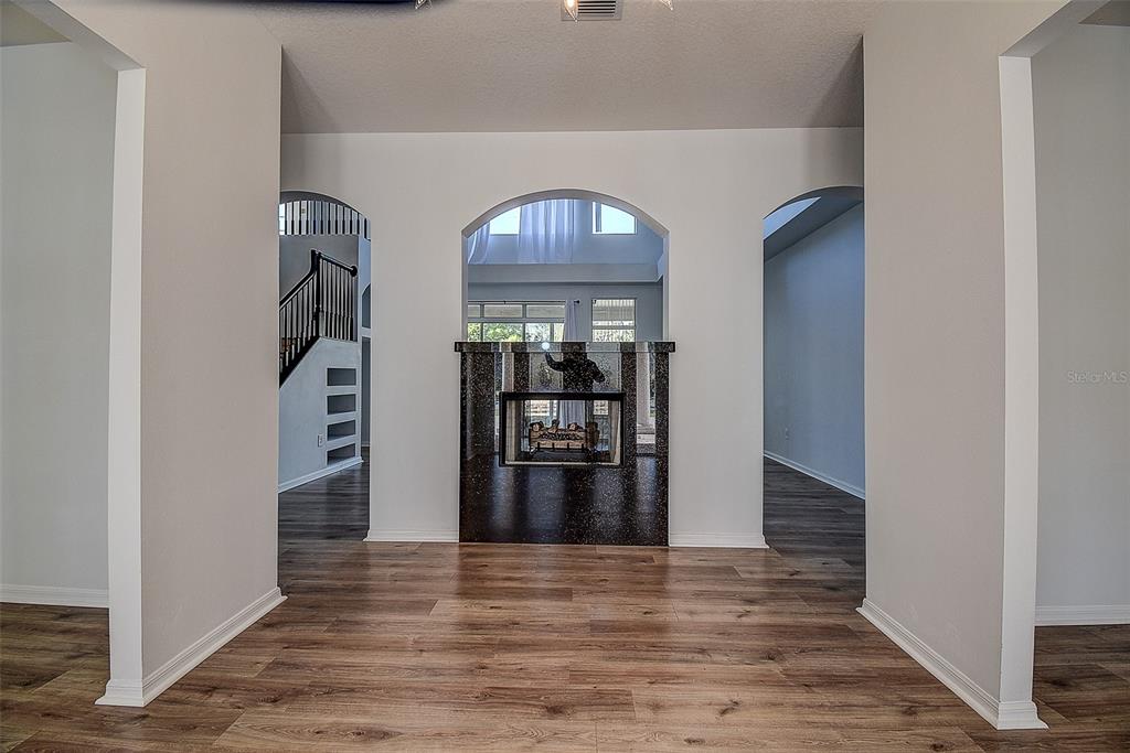A room with wood-look flooring features a central, dark-tiled fireplace under an arched opening — 15906 PRINCE WILLIAM PLACE, ODESSA, FL