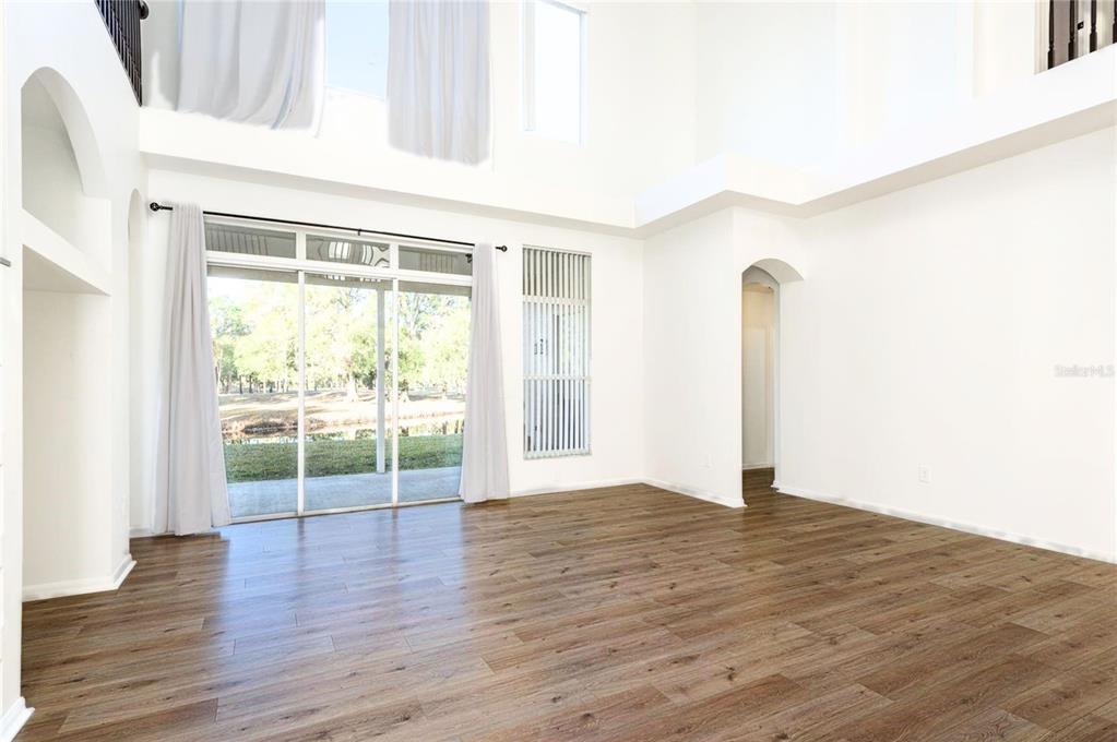 A bright, high-ceilinged living room features wood-look flooring, white walls, and large sliding glass doors — 15906 PRINCE WILLIAM PLACE, ODESSA, FL