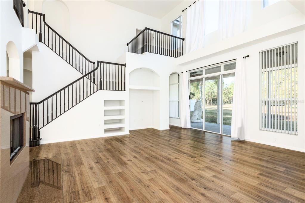 A spacious living room features wood-look flooring, a grand staircase, and large sliding glass doors — 15906 PRINCE WILLIAM PLACE, ODESSA, FL