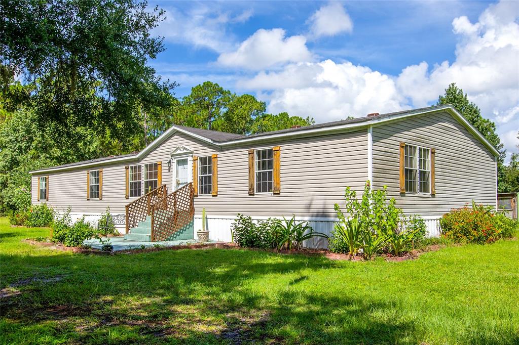 A single-story manufactured home with beige vinyl siding, a front porch, and surrounding green lawn — 104 EVERETT STREET, PALATKA, FL
