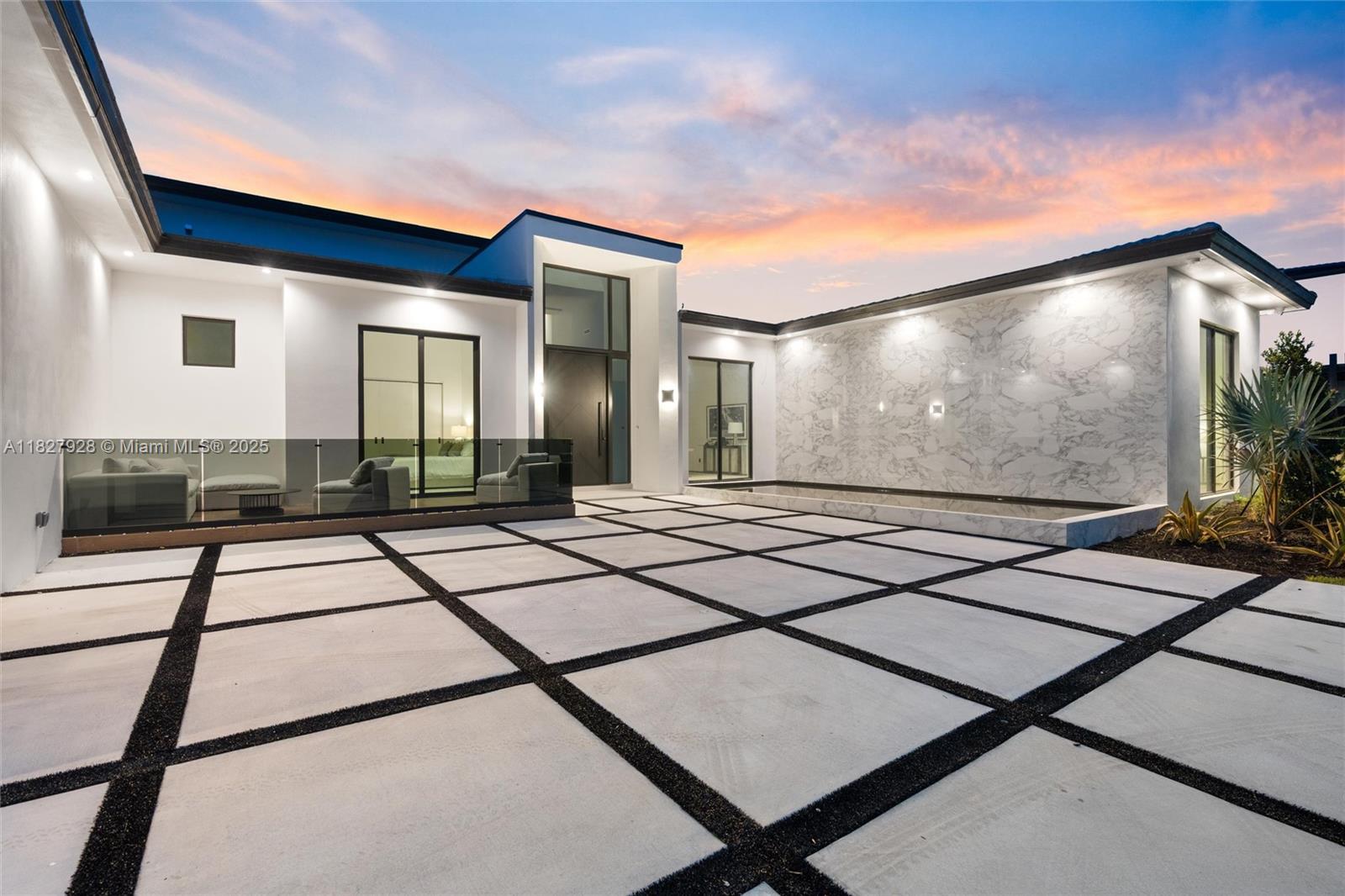 A modern house exterior features a grid-patterned concrete patio, marble wall, and glass entryway — 1520 SW 149th Ter, Davie FL 33326, DAVIE, FL