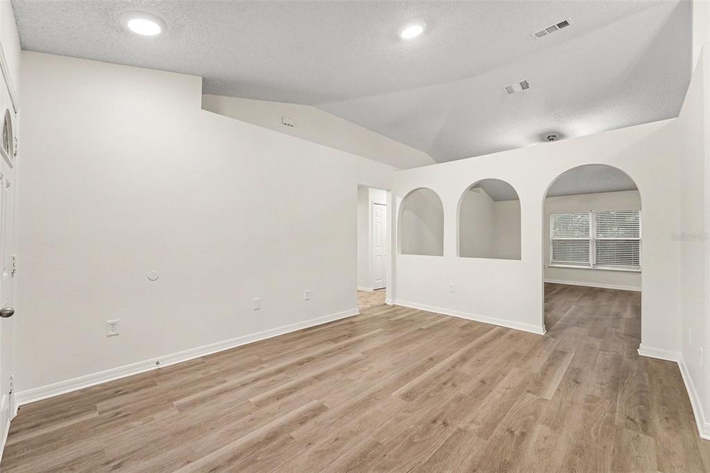 An empty room with light wood-look flooring, white walls, vaulted ceilings, and arched wall cutouts — 1228 WELCH RIDGE TERRACE, APOPKA, FL