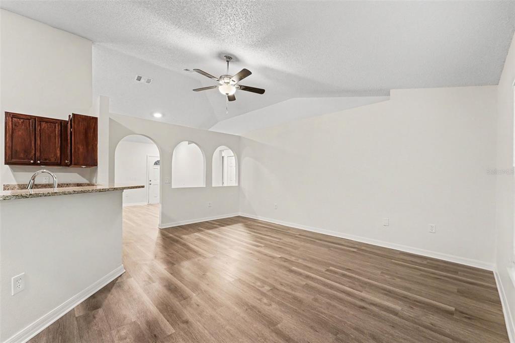 An open living area features wood-look flooring, a vaulted ceiling with a fan, and arched cutouts — 1228 WELCH RIDGE TERRACE, APOPKA, FL
