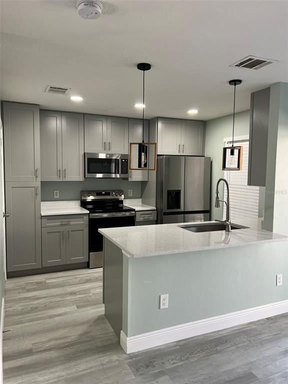 A kitchen features gray cabinets, stainless steel appliances, and a quartz-topped island with pendant lighting — 2906 CANDELA COURT, APOPKA, FL