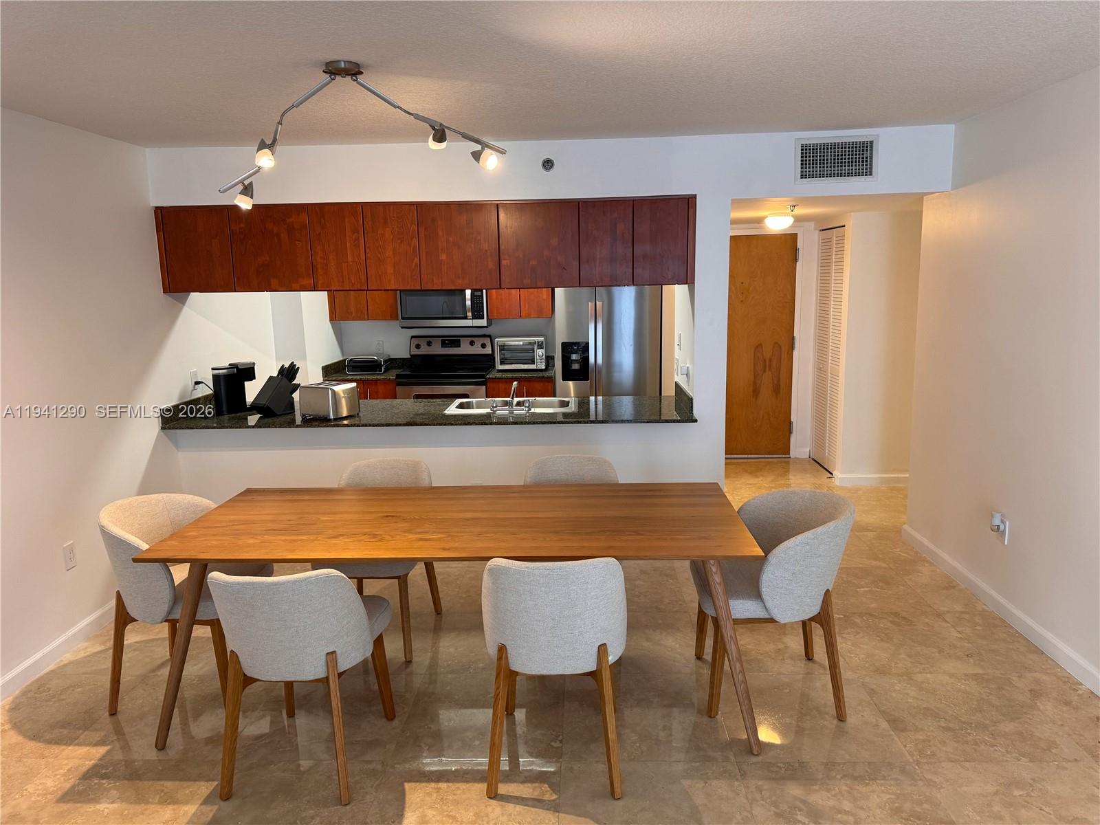 A dining area with a wooden table and six chairs sits before an open kitchen — 1200 Brickell Bay Dr # 1708, Miami FL 33131, MIAMI, FL
