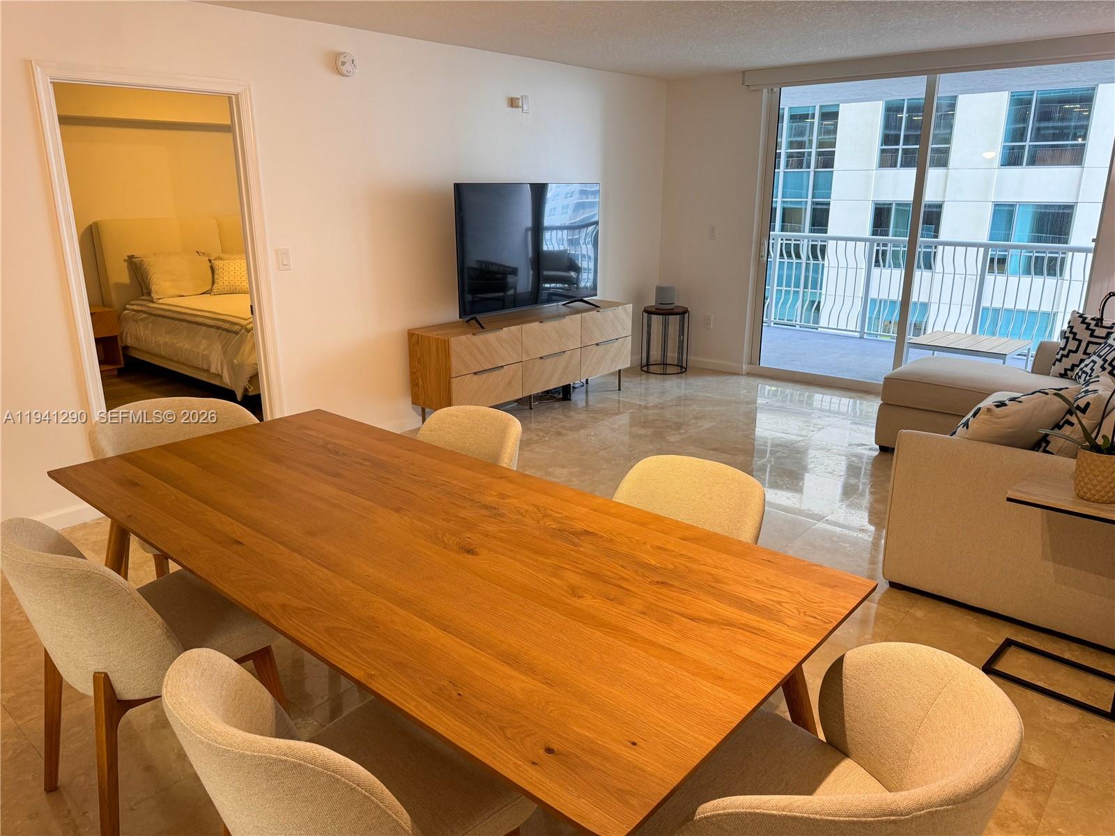 A dining area and living room feature light tile floors, a wooden table, and balcony access — 1200 Brickell Bay Dr # 1708, Miami FL 33131, MIAMI, FL
