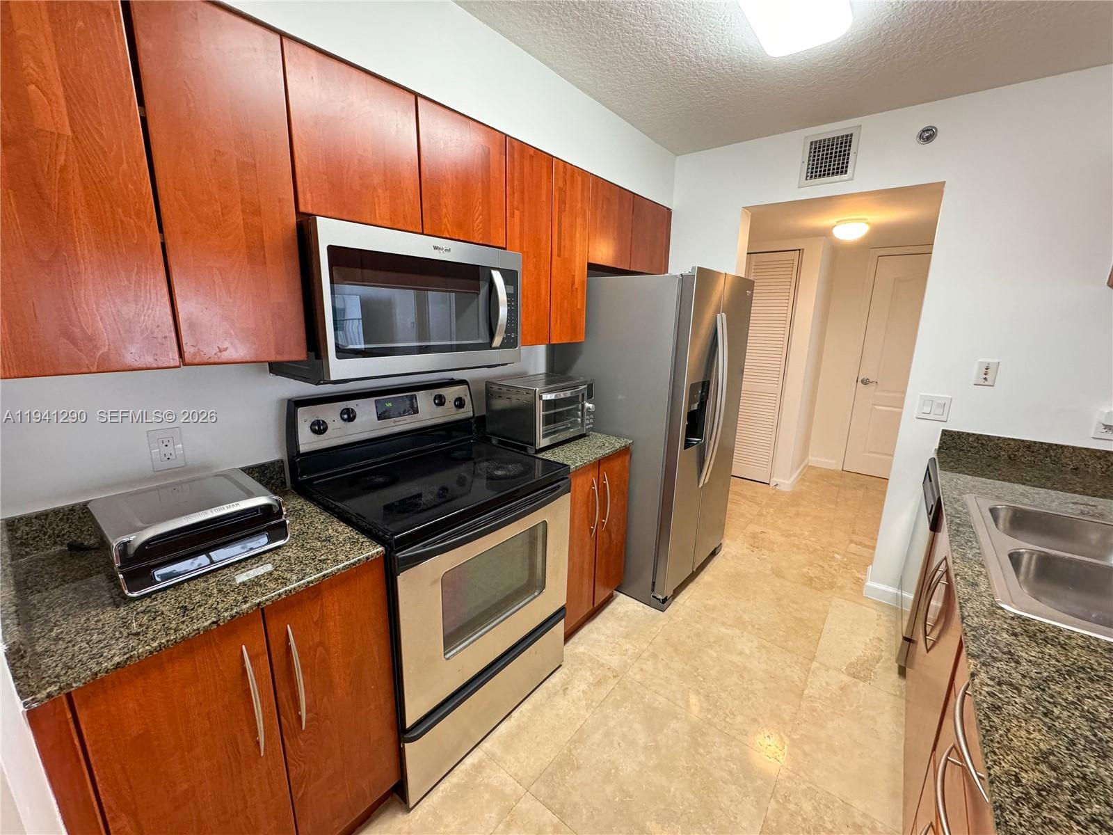 A kitchen features wood cabinets, granite countertops, stainless steel appliances, and light tile flooring — 1200 Brickell Bay Dr # 1708, Miami FL 33131, MIAMI, FL