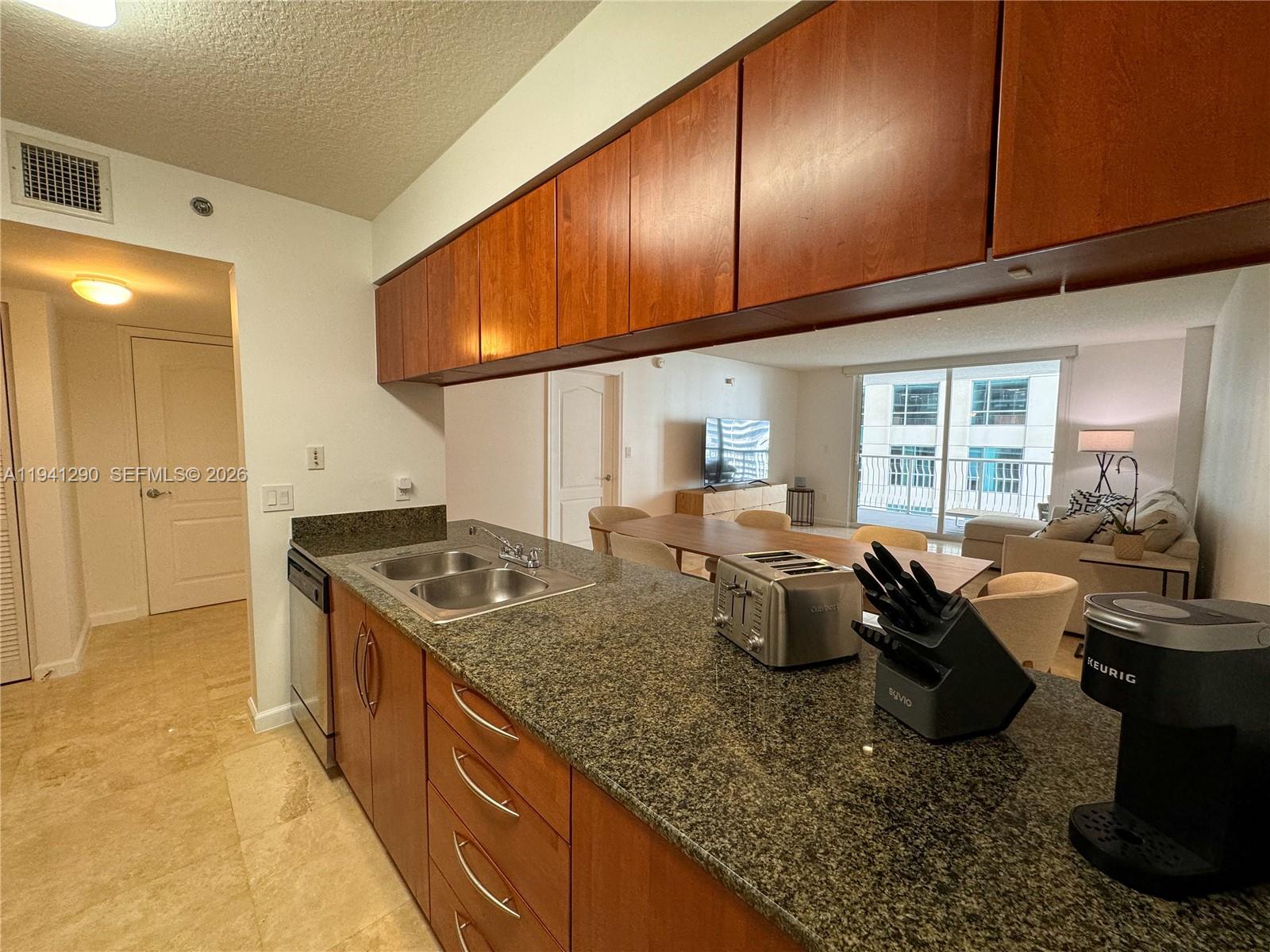 A kitchen with granite countertops and wood cabinets overlooks a dining and living area — 1200 Brickell Bay Dr # 1708, Miami FL 33131, MIAMI, FL