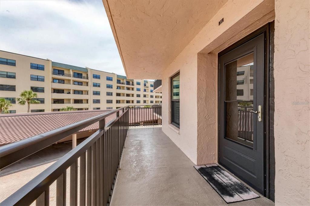 An outdoor balcony features a dark door, a metal railing, and a view of buildings — 6480 MIDNIGHT PASS ROAD UNIT 311, SARASOTA, FL
