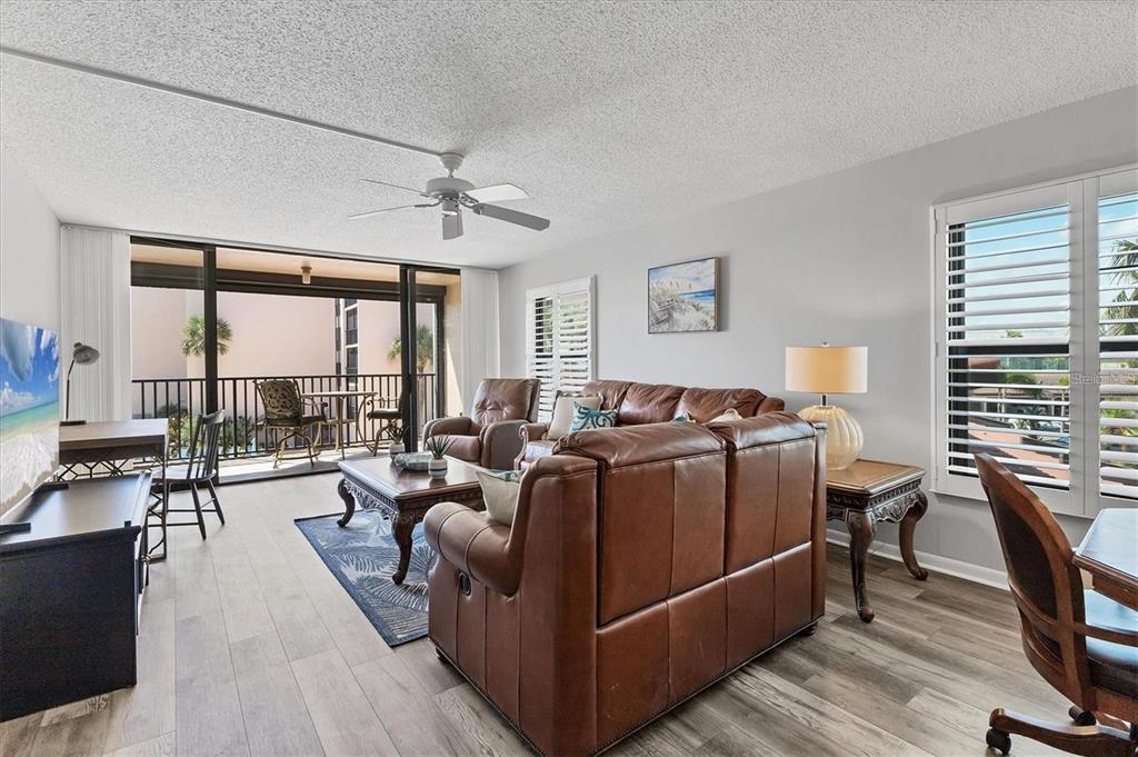 A living room features a brown leather sofa, wood-look flooring, and a balcony with outdoor seating — 6480 MIDNIGHT PASS ROAD UNIT 311, SARASOTA, FL
