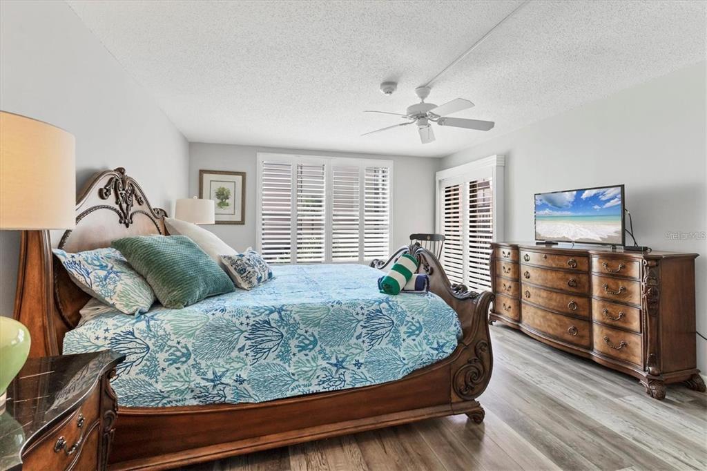 A bedroom features a wooden sleigh bed, a dresser with a television, and plantation shutters — 6480 MIDNIGHT PASS ROAD UNIT 311, SARASOTA, FL